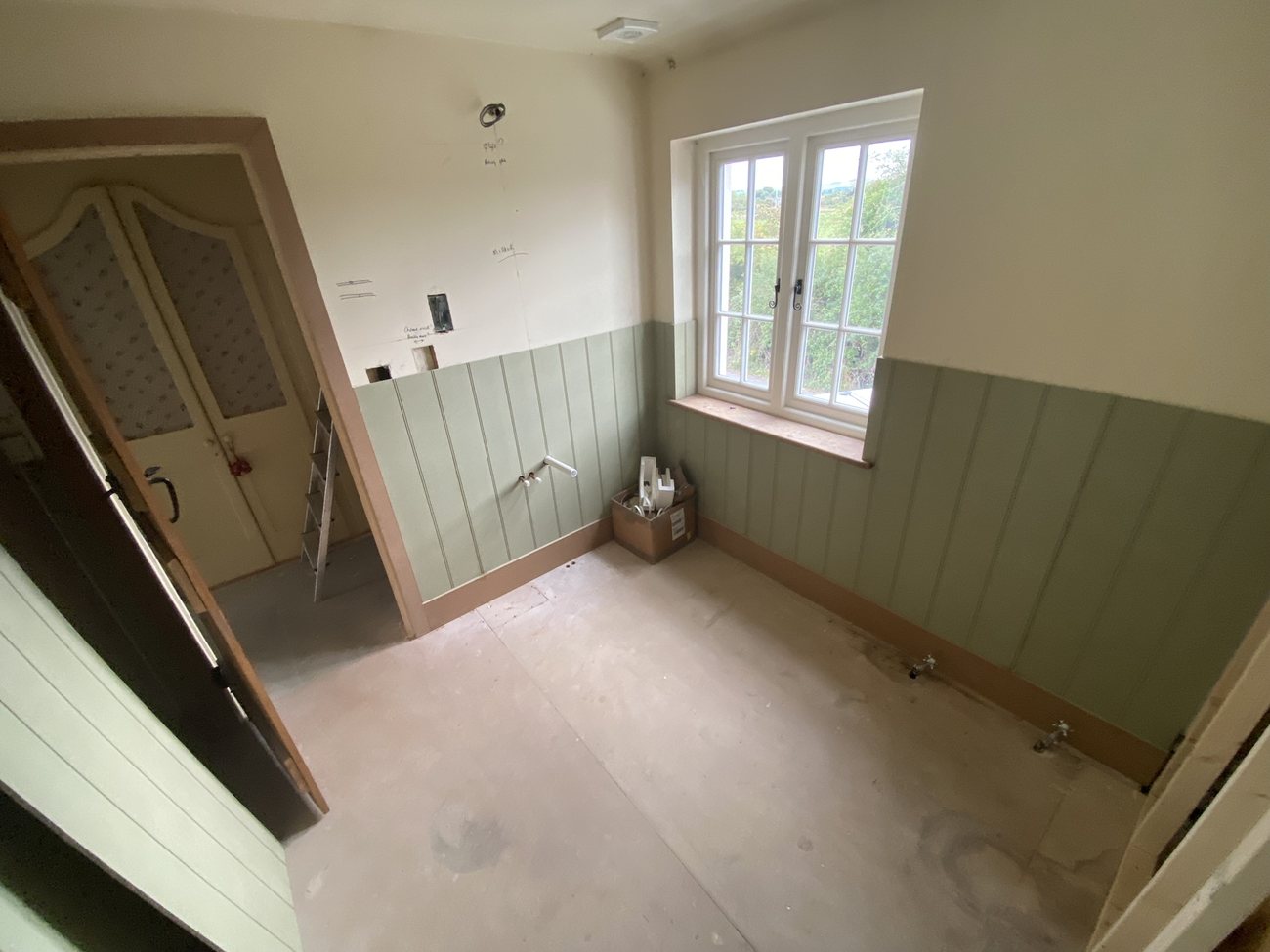 Room with sage green wall panelling and an oak door